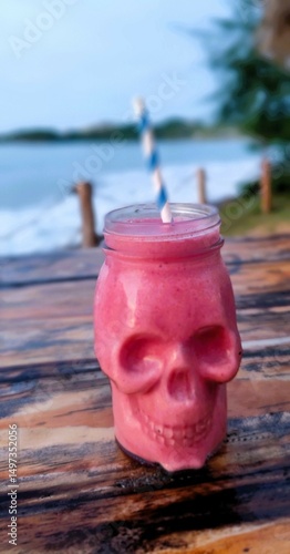 Tropical pink smoothie in skull-shaped glass with straw by the beach