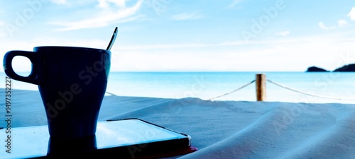 Coffee mug on tablet on Balinese daybed overlooking turquoise sea