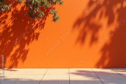 A vibrant orange wall with leaf shadows and a tree branch casting shadows on a tiled surface