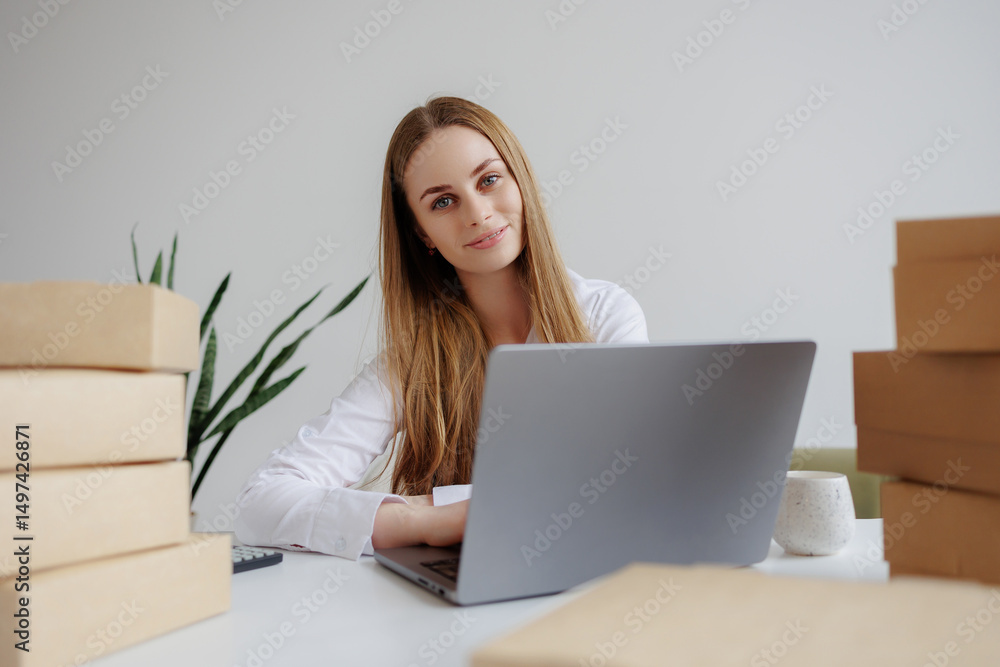 © Sandu - Young businesswoman working at her desk surrounded by boxes and a plant in a light office environment