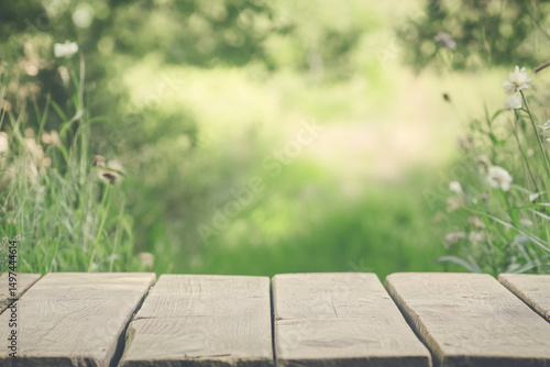 A serene wooden pathway leading into a lush green landscape, surrounded by soft-focus wildflowers and grass, creating a tranquil outdoor scene.