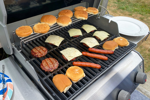 Barbecuing hot dogs and hamburgers on the grill. Grilled cheese burgers hot dogs and buns over open flame. Summer barbecue