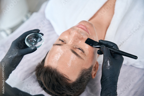 Quadro su tela Cosmetologist applying facial peeling mask with retinol for man