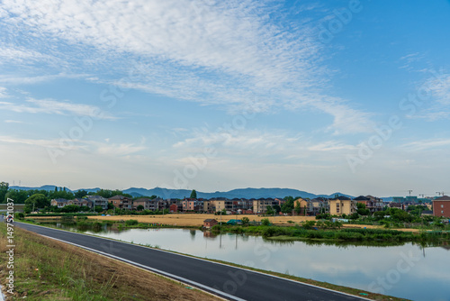 Residential houses along a riverbank under a blue sky with clouds.