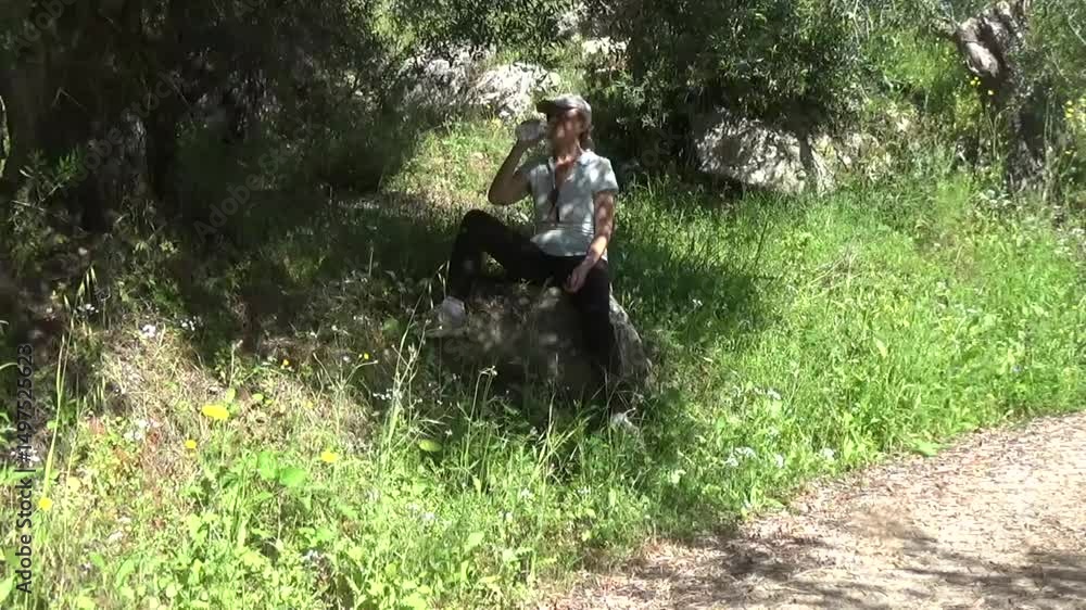 A girl drinks water in the forest. She is resting on a big rock under a tree and drinks water from a bottle. Weekend mountain hike A girl drinks water in the forest. She is resting on a big rock under a tree and drinks water from a bottle. Weekend mountain hike