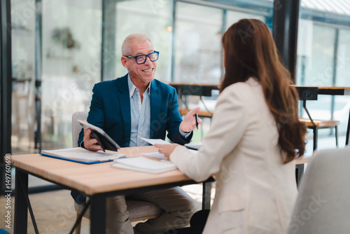 Senior manager explaining marketing strategy to his young female colleague during a business meeting in a modern office, they're analyzing financial reports using a tablet and paper documents