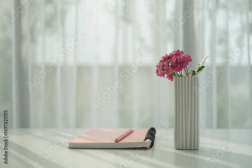 Pink notebook and rose, by the window with white curtain, cozy workspace