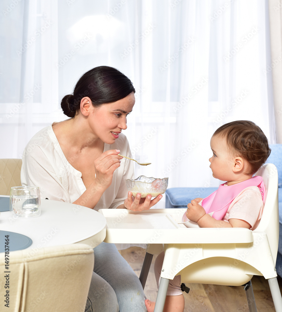 Mother feeding baby with a spoon. Spoon-feed. Happy young mother with a baby in the kitchen interior. Fresh vegetables and fruits. Mother feeding baby with a spoon. Spoon-feed. Happy young mother with a baby in the kitchen interior. Fresh vegetables and fruits.