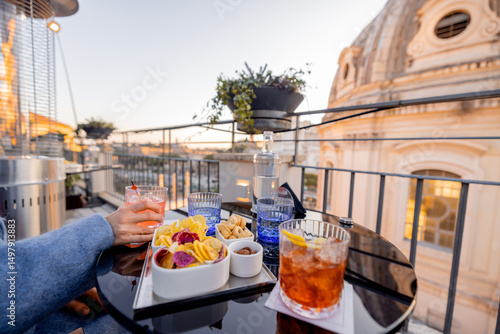 Fotografie Elegant aperitivo with cocktails and snacks on a Roman rooftop at sunset