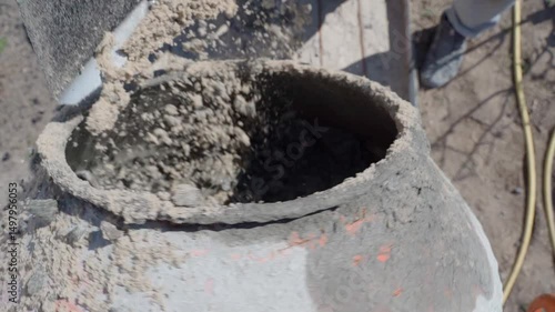 A shovelful of sand is being thrown into a rotating concrete mixer, close-up, top view