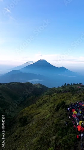 A panoramic view of a mountain range with lush green hills, a distant peak shrouded in mist, and a clear blue sky
