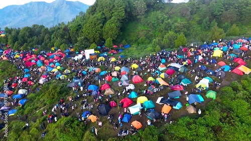 A vast campsite sprawls across a mountainside, filled with colorful tents and numerous people enjoying the outdoors