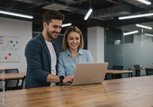 Two colleagues working together on a laptop in a modern office space