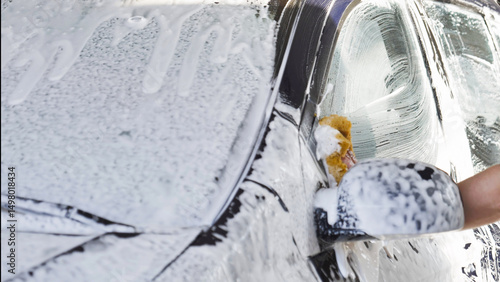 Car wash worker cleaning vehicle with sponge and soap