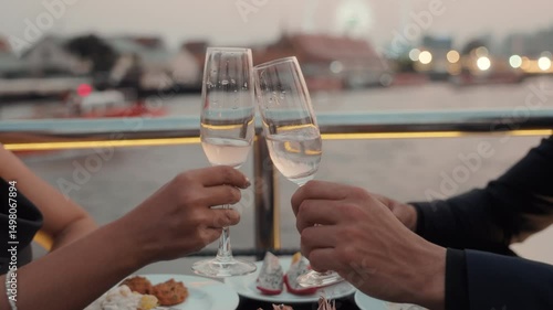 Romantic partners hands clink glasses of expensive wine on dinner riding luxury yacht closeup. Young couple celebrates anniversary sailing modern ship on sea journey in evening