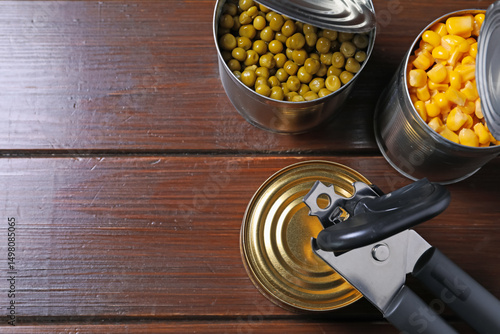 Foto Can opener and tins with products on wooden table, flat lay