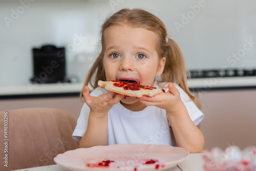 Cute blonde girl eating waffles with jam at home in the kitchen