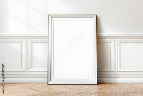 Vertical blank frame mockup with gold trim leaning against an ornate white wall in a classic interior - ideal for showcasing artwork, posters, or elegant branding presentations