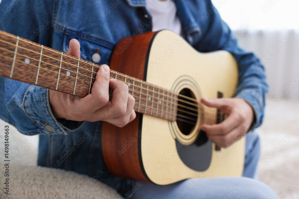 Fototapeta premium Man playing guitar on armchair indoors, closeup