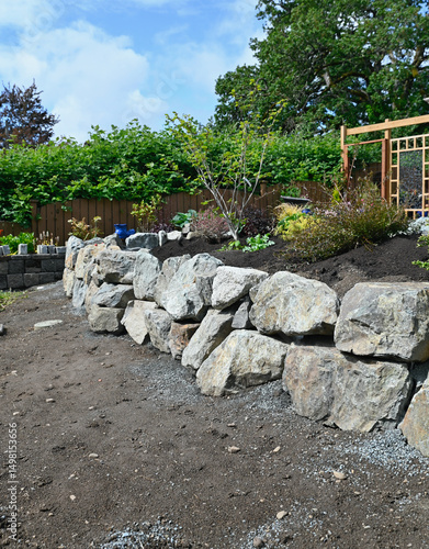 Landscape design project of stacked stone wall in progress in yard and garden