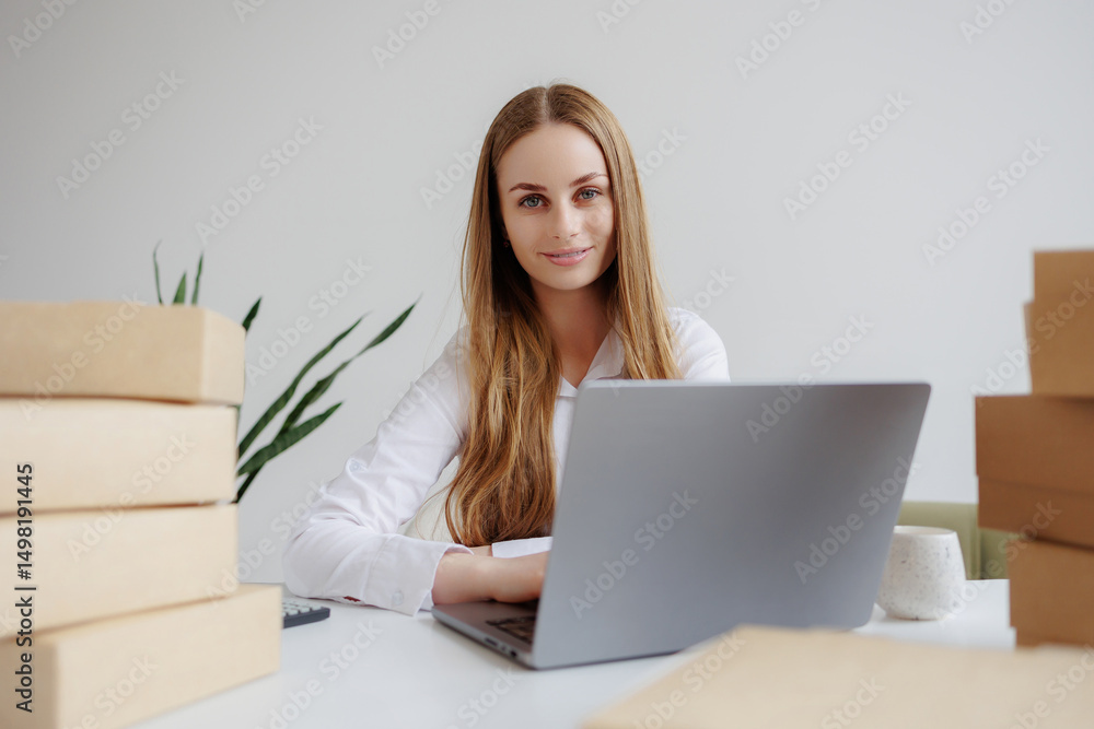 Woman working on laptop surrounded by packaged boxes in a modern office space during daytime Woman working on laptop surrounded by packaged boxes in a modern office space during daytime