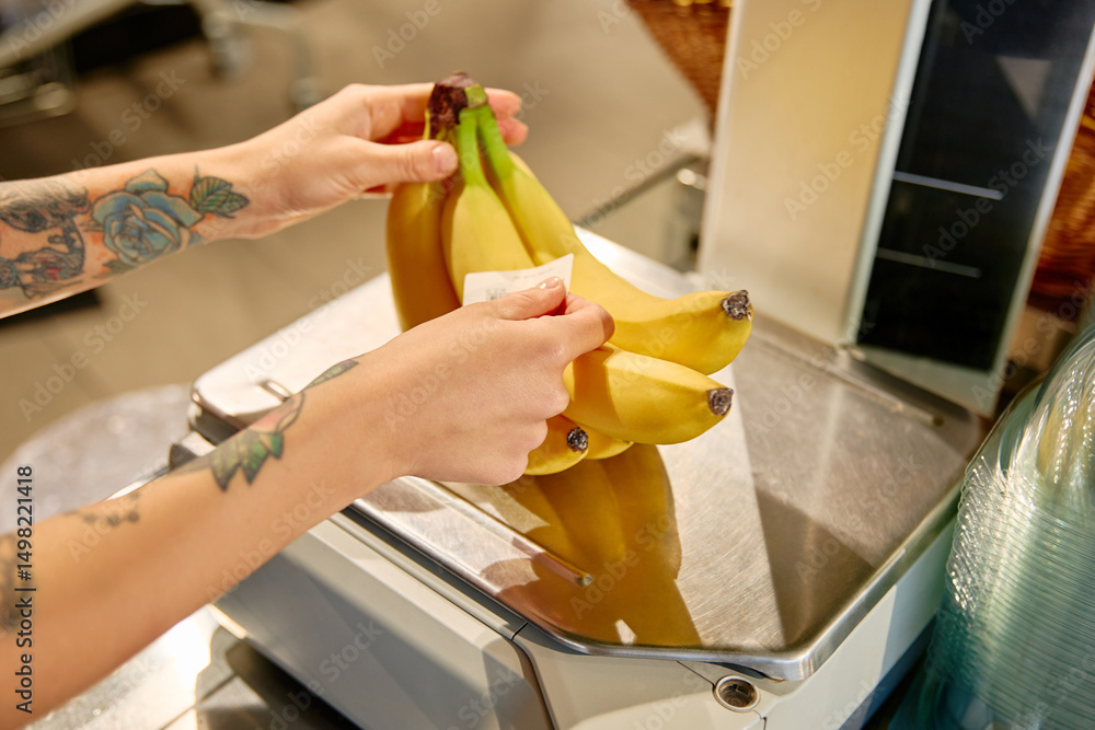 Obraz na plátně Grocery store worker weighing bananas at checkout scale