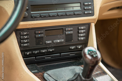 Center dash panel of a 2000s european luxury car. Dual-zone AC, seat heat and massage, vent direction. Pixel displays, wood trim, optional radio, cup holders. Manual gear. Beige interior.