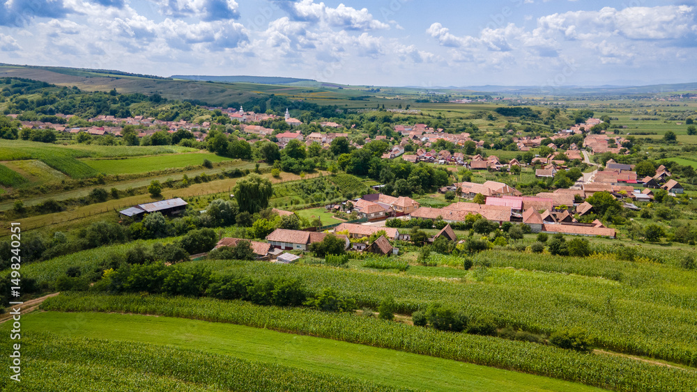 Fototapeta premium Picturesque romanian village with red roofs surrounded by cultivated fields under a cloudy sky