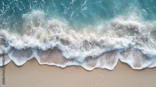 Aerial view of gentle ocean waves rolling onto a sandy beach, creating foamy patterns along the shoreline