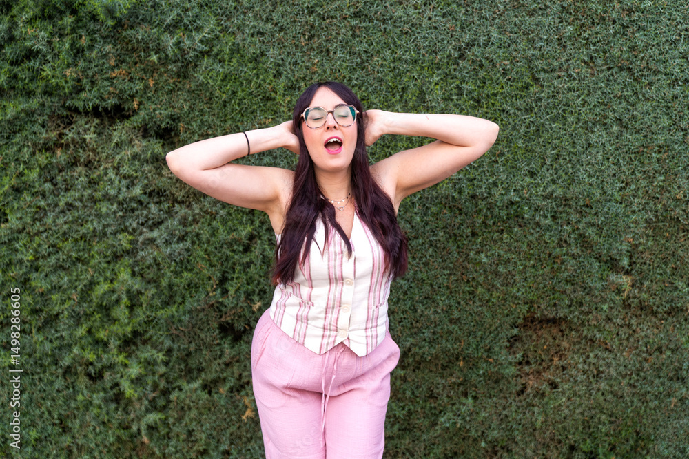 Young woman wearing pink linen outfit and singing with hands on headset Young woman wearing pink linen outfit and singing with hands on headset