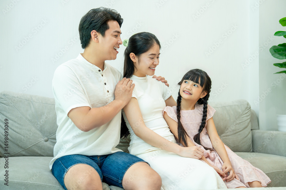 Asian family (father, daughter, and mother) sitting on a sofa, looking at each other and smiling. Asian family (father, daughter, and mother) sitting on a sofa, looking at each other and smiling.