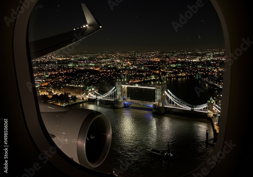 The illuminated Tower Bridge of London, captured from an airplane window on a night flight over the city.