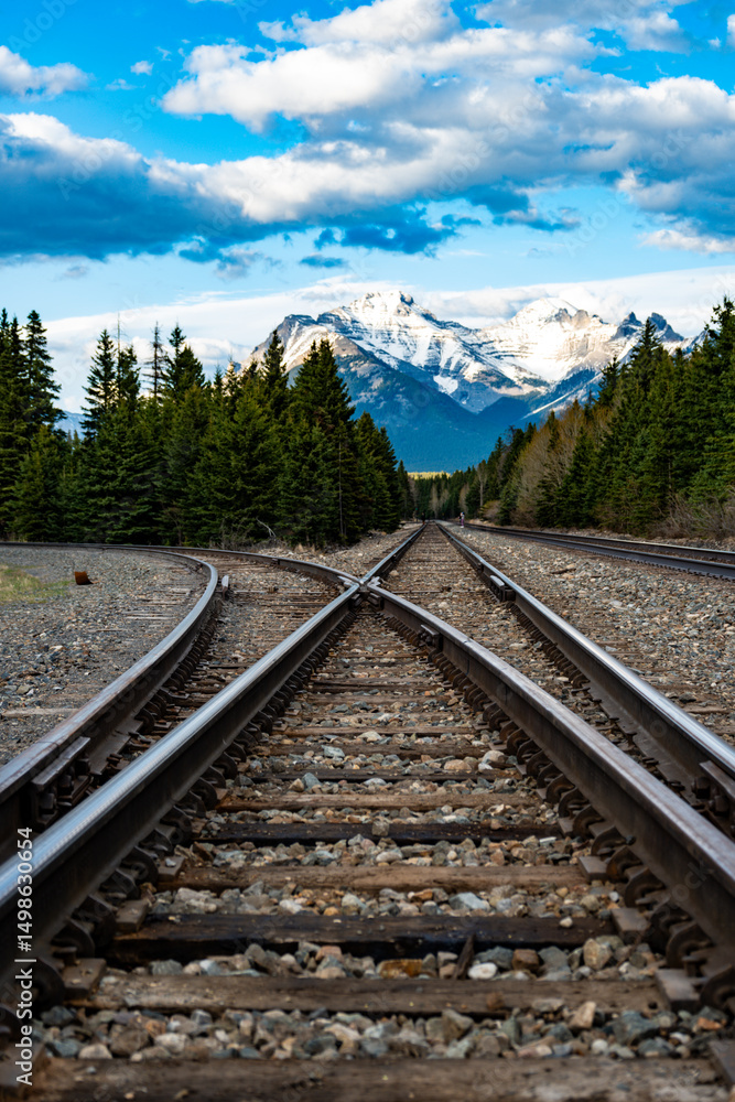 Obraz premium Converging train tracks with mountains and clear blue sky in the background