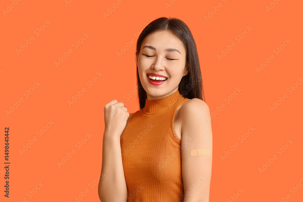 Obraz premium Happy Asian woman with applied medical patch on orange background. Immunization concept