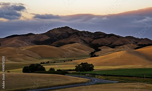 Rolling hills bathed in the golden light of sunset, a lone road winds through the landscape