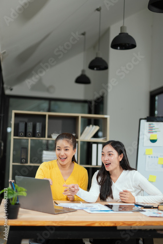 Group of happy Asian business people having a meeting at the office. Two women working together using modern laptops.