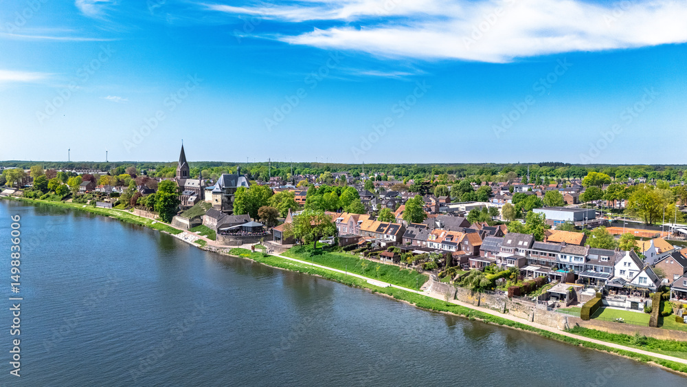 Naklejka premium Aerial drone view of typical Dutch village, idyllic countryside landscape with traditional houses and church near river Meuse in spring, Limburg province, the Netherlands