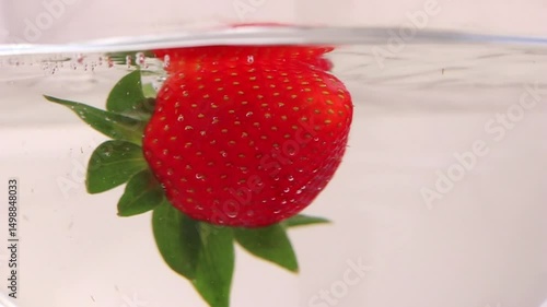 Strawberry slowly splash into water. Fresh summer berry