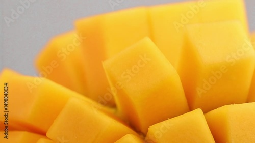 A diced mango half slowly rotates in a circle. The juicy tropical fruit is ready for smoothies, cocktails and desserts. Yellow juicy cubes of pulp