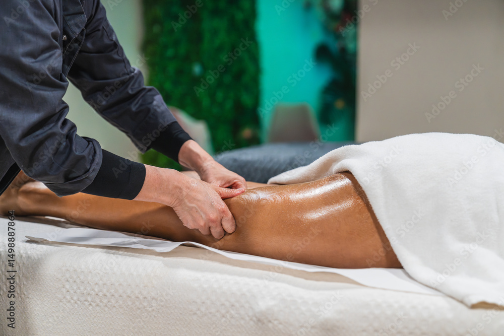 Fototapeta premium Professional physiotherapist giving a leg massage to a young woman lying on a massage table in a modern spa center