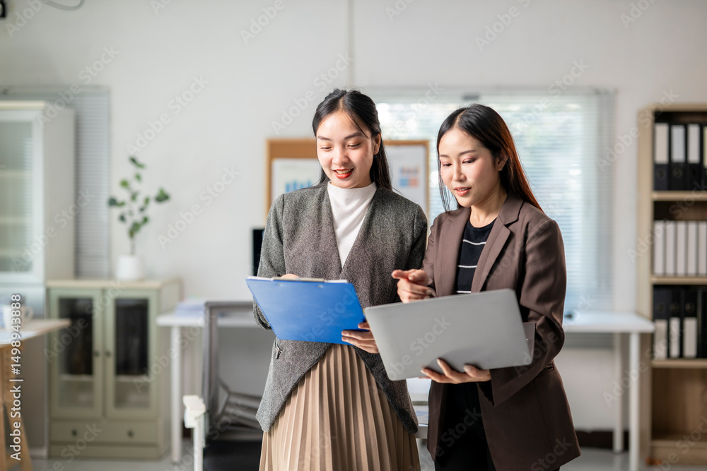 Two women in business attire are looking at a laptop together Two women in business attire are looking at a laptop together