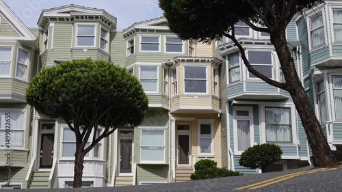 Colorful Victorian-style houses on a steep street with manicured trees in front, typical of San Francisco

