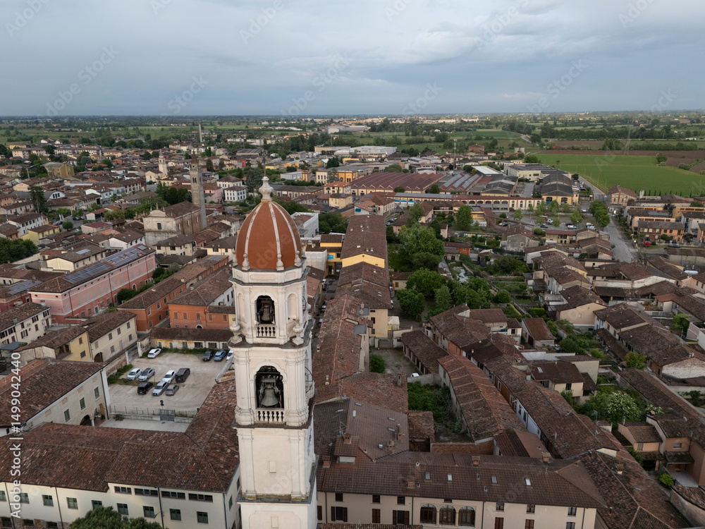 Obraz premium Aerial drone view of Abbazia dei Santi Tommaso e Andrea Apostoli bell tower rising above terra-cotta rooftops in Pontevico, Brescia Italy