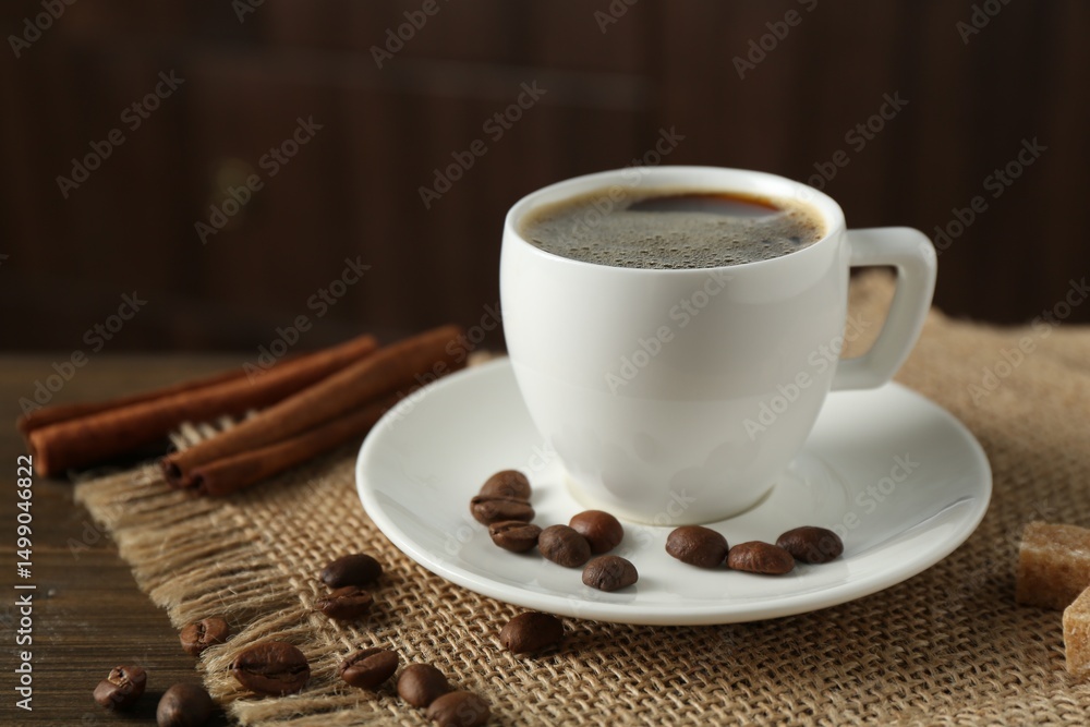 Fototapeta premium Aromatic coffee in cup, beans, brown sugar and cinnamon on wooden table, closeup