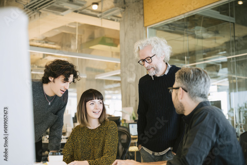 Midday in an open office space with neutral tones A multigenerational team is gathered around a desk, discussing ideas and sharing