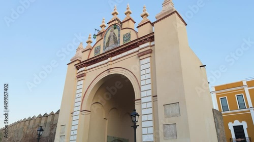 Frontal view of the historic yellow arch of La Macarena, with its symmetrical silhouette and white moldings framing one of the ancient gates of Seville’s city wall. A symbol of Andalusian architectura