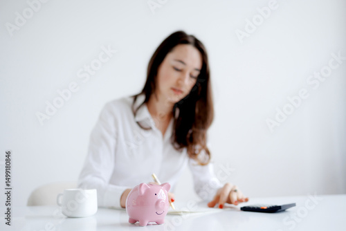 Woman managing finances at a white desk with a piggy bank and calculator in a bright and minimal workspace