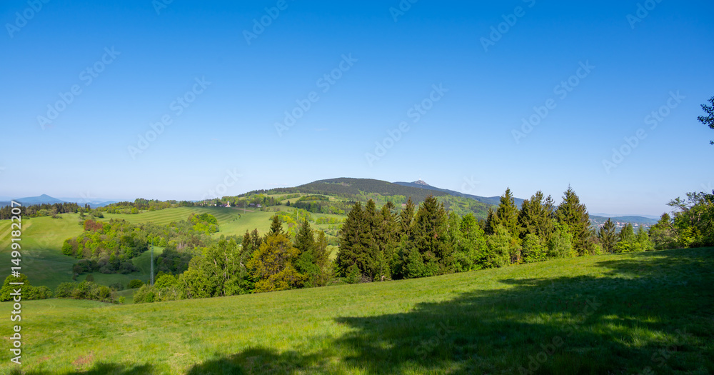 Obraz premium Panoramic view of Jested mountain with its iconic tower on the top, surrounded by green meadows, scattered cottages and small villages in the Czech countryside
