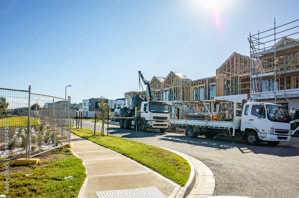 Fototapeta premium Construction site with wooden frame houses under development in suburban Melbourne Australia, featuring delivery trucks, scaffolding, and residential building infrastructure