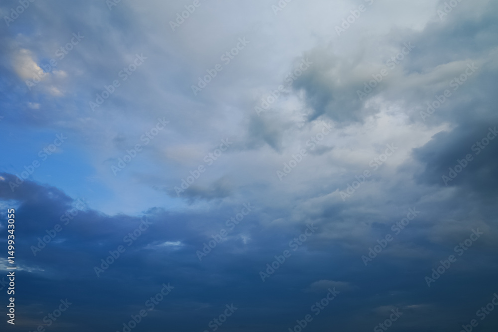 Obraz premium Dark storm clouds gather across the blue sky during the rainy season, forming dramatic shapes as nature signals an approaching storm over the open landscape.